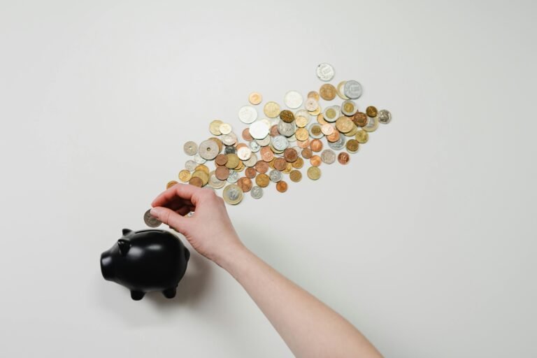 How to Build a Super-Powered Solo 401(k) in 2026 Person placing coin into a black piggy bank with scattered coins, symbolizing savings and finance.
